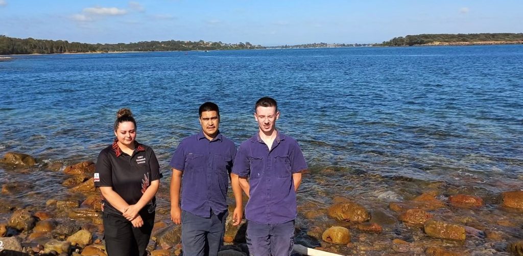 Three Indigenous Rangers standing at the shoreline.